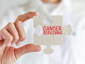 Businesswoman holding jigsaw puzzle pieces with “Cancer screening” text